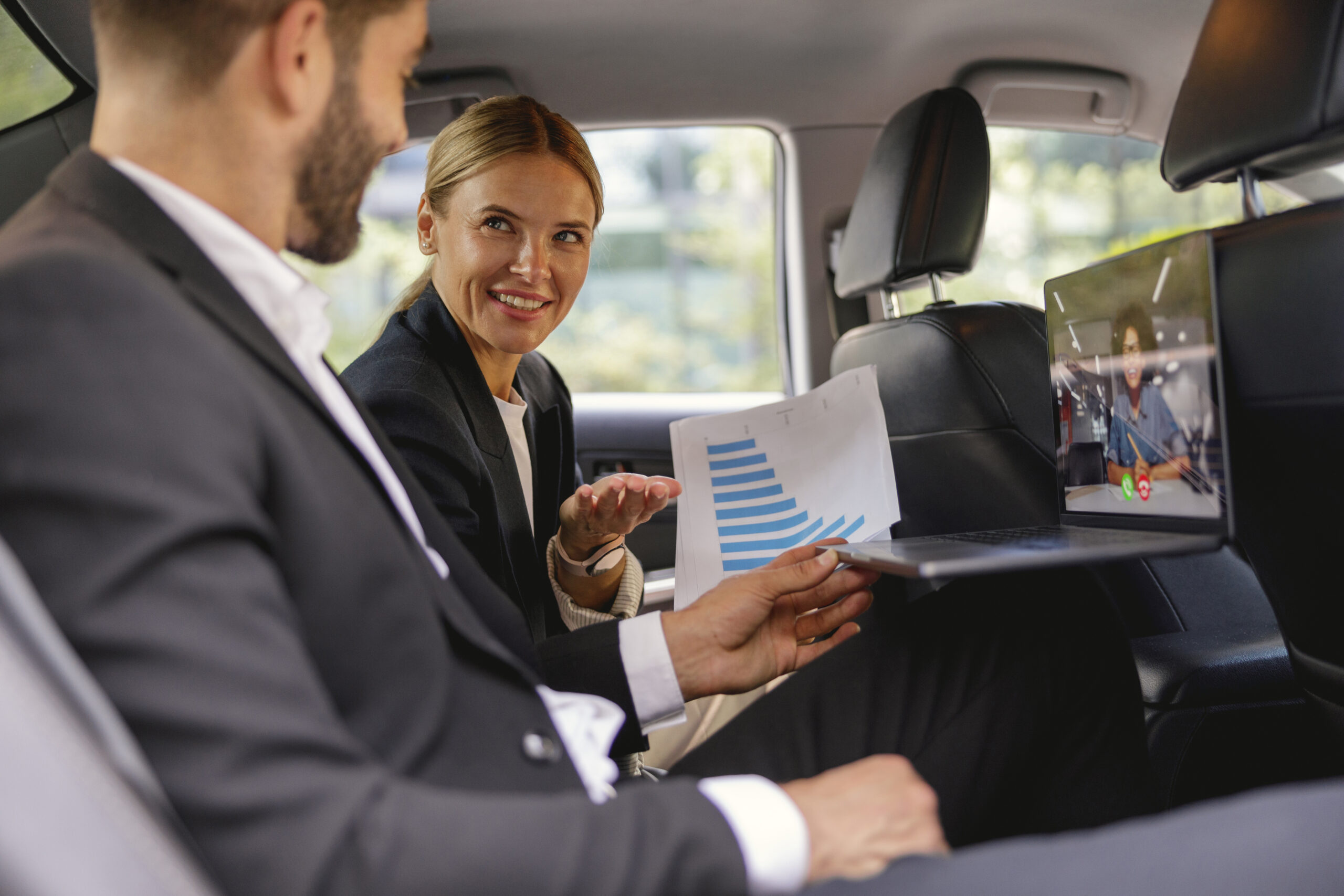 Clients en déplacement professionnel travaillant à l’arrière d’une berline avec chauffeur privé