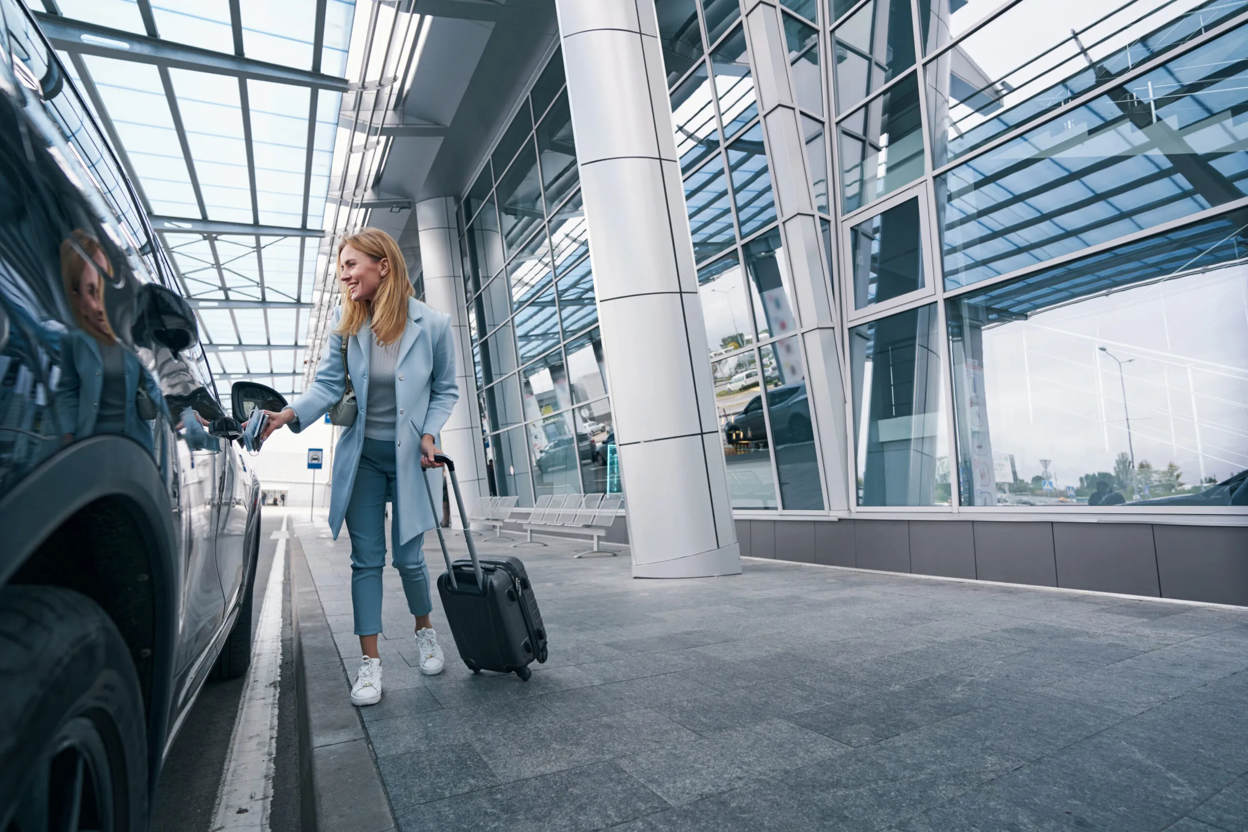 Femme avec valise montant dans une berline devant un terminal pour un transfert aéroport privé
